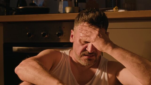 Middle aged Caucasian man holding wedding ring, crying in despair and suffering from addiction. Useful for mental health awareness, substance abuse recovery, divorce counseling campaigns