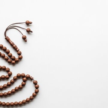 Brown wooden tasbih prayer beads with carved tassel and decorative accents on a white background with negative space. Traditional misbaha used for Islamic dhikr, meditation and prayer.