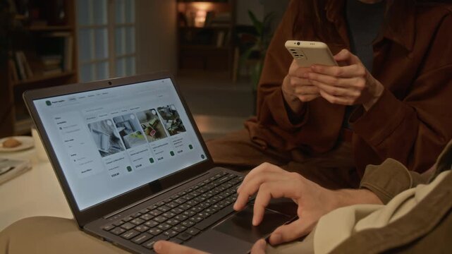 Young couple browsing e-commerce store catalog using laptop and smartphone at home. Footage suitable for marketing digital retail platforms, mobile applications, and consumer tech