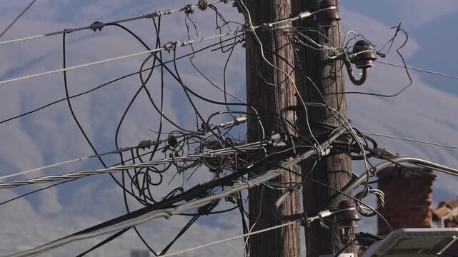 A power line with a lot of wires hanging from it. The wires are tangled and twisted. The image has a mood of chaos and disorder
