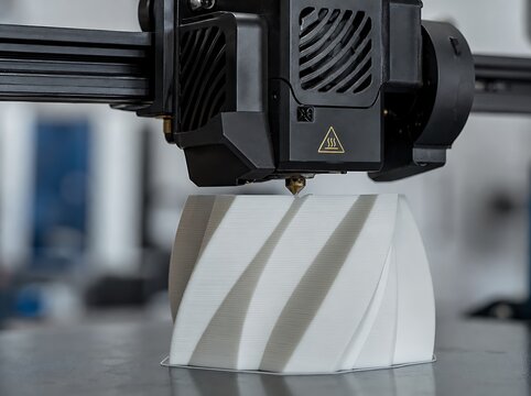Automated three dimensional printer creating white spiral geometric prototype in workshop facility.