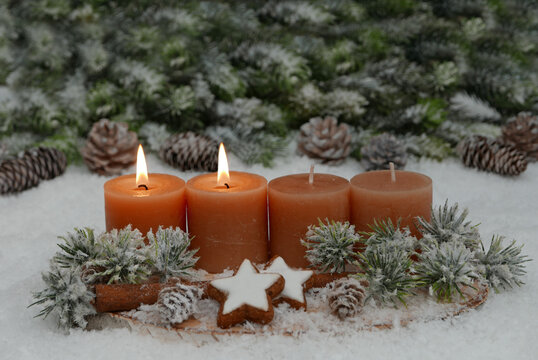 Nat&uuml;rliches Adventsgesteck auf einer Holzscheibe im Schnee.  Zwei Kerzen brennen f&uuml;r den 2. Advent.