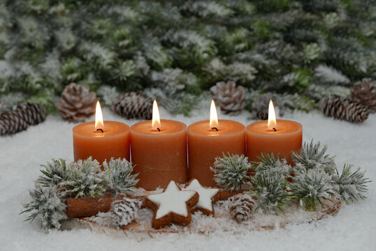 Nat&uuml;rliches Adventsgesteck auf einer Holzscheibe im Schnee. Vier Kerzen brennen f&uuml;r den 4. Advent.
