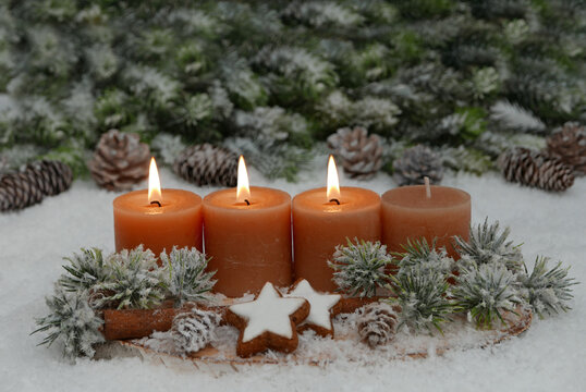 Nat&uuml;rliches Adventsgesteck auf einer Holzscheibe im Schnee.  Drei Kerzen brennen f&uuml;r den 3. Advent.