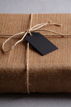 Rustic gift box wrapped in burlap fabric and tied with twine string featuring a dark label tag
