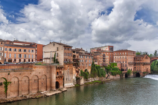 View of old brick houses on the opposite bank of Tarn river in Albi, France. Historic urban architecture under sky