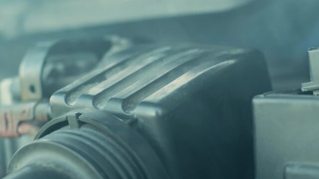 Handheld slow motion shot of engine bay showing smoke drifting around a plastic air intake housing, suggesting overheating or mechanical trouble for auto repair themes.