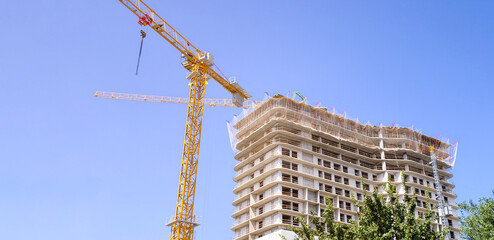 Modern high rise building under construction with a towering yellow crane against a clear blue sky, symbolizing growth, development, and urban expansion © Newleks