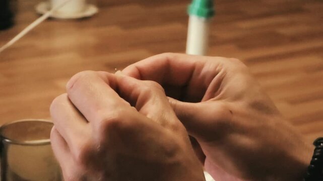 Hands threading needle at craft workshop table. Close up of man learning sewing skill during handmade lesson. Traditional handicraft and needlework education concept.