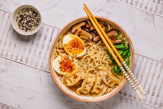 Bowl of noodles with dumplings, egg, and mushrooms on a wooden table