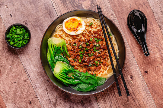 A bowl of noodles with minced meat, egg, and bok choy.