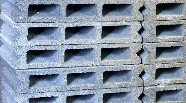 Stacked grey concrete hollow blocks with rectangular holes and interlock grooves close up view durable cement cinder blocks building construction material texture background for masonry architecture.