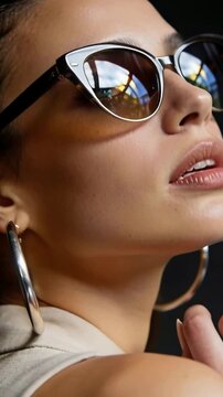 Vertical video: Reacting to hand entry, model fixing earring in studio for pose, cat-eye shades lit