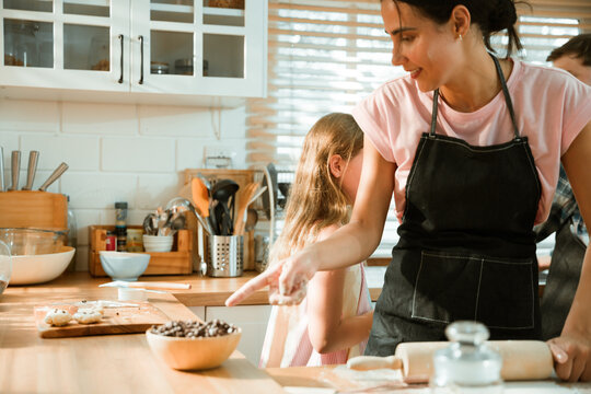 Family cooking concept with parents and daughter preparing homemade food together in a bright kitchen, sharing baking skills and quality time. family, cooking, kitchen, baking, together
