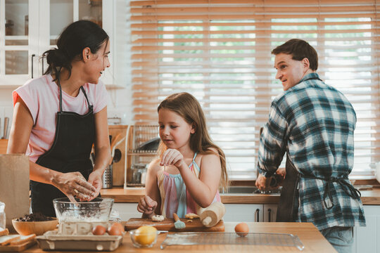 Family cooking concept with parents and daughter preparing homemade food together in a bright kitchen, sharing baking skills and quality time. family, cooking, kitchen, baking, together