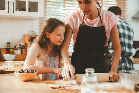 Family cooking concept with parents and daughter preparing homemade food together in a bright kitchen, sharing baking skills and quality time. family, cooking, kitchen, baking, together