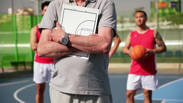 Serious basketball coach with a clipboard standing in front of his players on an outdoor court