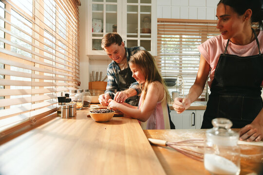 Family cooking concept with parents and daughter preparing homemade food together in a bright kitchen, sharing baking skills and quality time. family, cooking, kitchen, baking, together