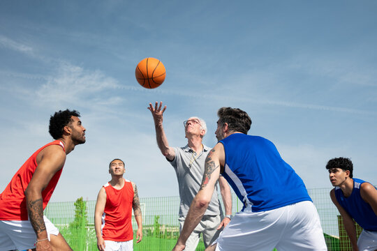Players anticipating the jump ball to start a lively outdoor basketball game