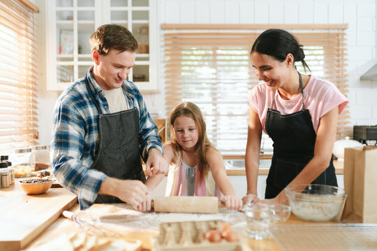 Family cooking concept with parents and daughter preparing homemade food together in a bright kitchen, sharing baking skills and quality time. family, cooking, kitchen, baking, together