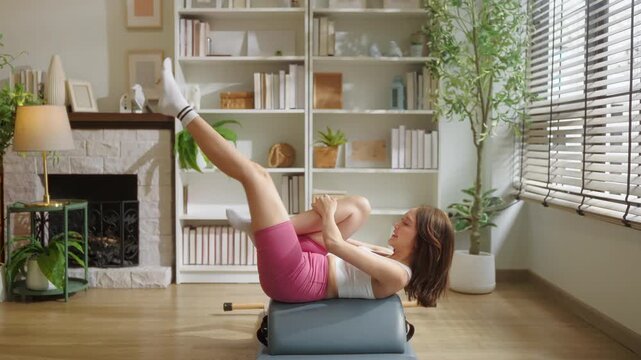 Woman practicing Pilates on a spine corrector, legs extended upward in a controlled stretch, bright minimalist studio with natural light and green plants in the background.	