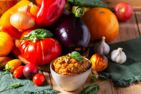 Eggplant caviar in a glass jar and vegetables on a wooden background.