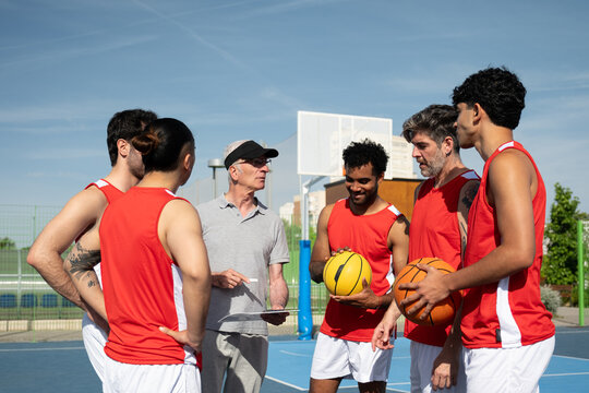 Basketball coach giving instructions to diverse team of players on an outdoor court