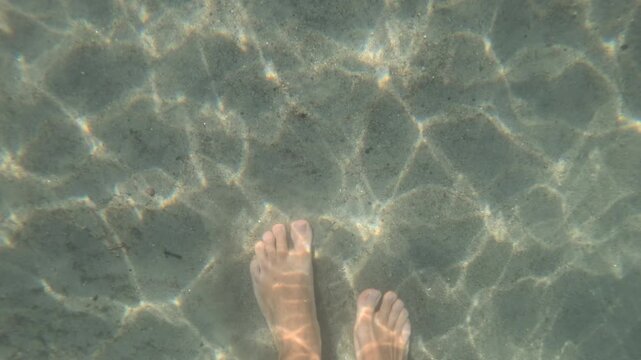 Underwater view of a swimmer's foot over rippled sand with sunlight patterns, Golfe-Juan, France