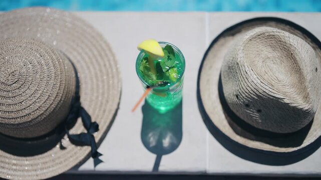 A green cocktail drink in a glass sits on pool edge next to a straw and a straw wrapper
