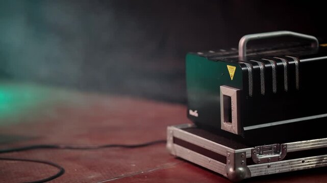 A black box with a yellow handle sits on a red surface. The box is emitting smoke, creating a mysterious and eerie atmosphere