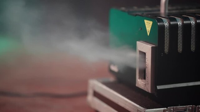 A black box with a yellow handle sits on a red surface. The box is emitting smoke, creating a mysterious and eerie atmosphere