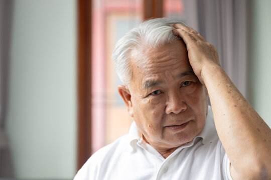 elderly asian man touching his grey hair with thoughtful expression, closeup portrait in soft natural light
