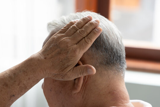 elderly asian man from behind touching his grey hair in a living room during daytime