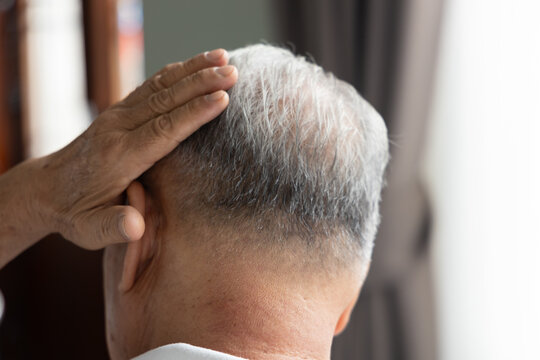 elderly asian man from behind touching his grey hair in a living room during daytime