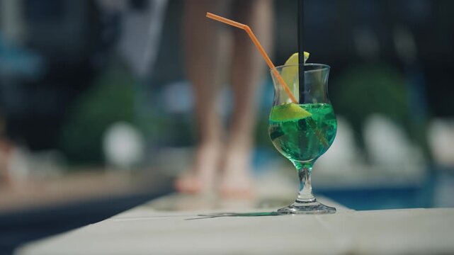 Fashion model female walk on pool edge, focused green cocktail drink in a glass with a straw in it, slow motion, summer vacation concept
