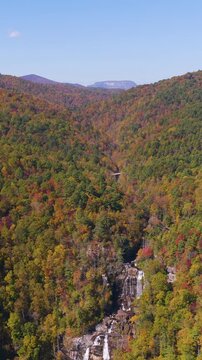 Aerial view of powerful waterfall cascading through lush forest. Colorful autumn foliage creates breathtaking wilderness landscape.
