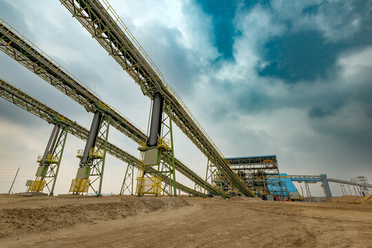 Large conveyor belts transport mineral ore directly into the crushing plant of an open copper mine facility, showcasing heavy industrial processing machinery and massive steel infrastructure.