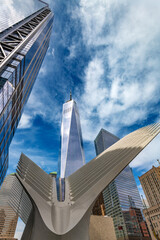 Obraz premium Looking up at the futuristic white architecture of the Oculus station and One World Trade Center rising into the sky among modern financial district skyscrapers in downtown Manhattan, New York City.