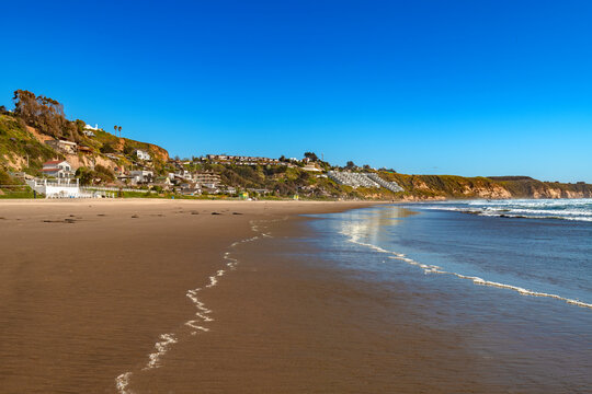 Scenic view of the coastal beach resort of Maitencillo in Chile, showcasing a wide sandy shore along the Pacific Ocean with residential houses and apartments built on hillside cliffs.