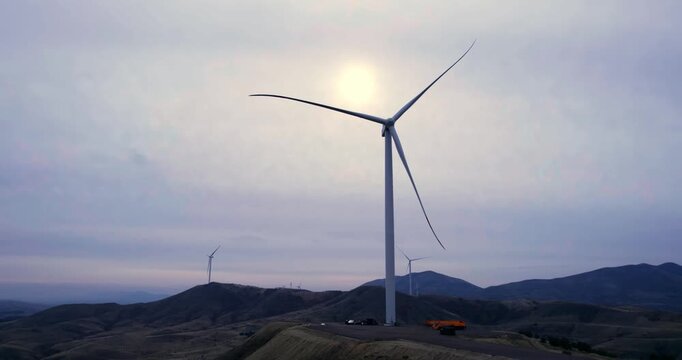 A wind turbine is standing tall on a hill. The sky is cloudy and the wind is blowing