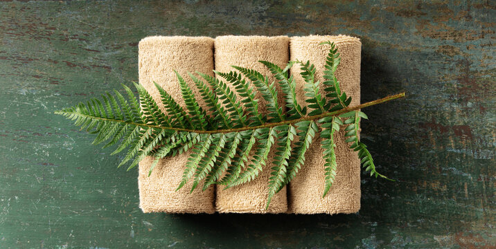 Natural Spa Towels with Green Fern Leaf on Rustic Wooden Background