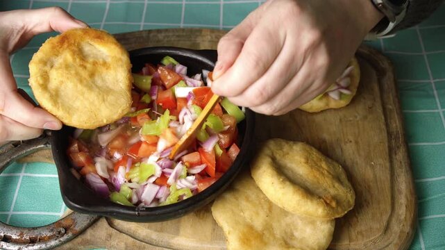 Close up of hands eating homemade sopaipillas with fresh tomato and onion pebre, High angle shot of hands enjoying fried sopaipillas topped with fresh pebre