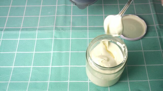 Hand carefully spooning fresh homemade mayonnaise into a clear glass jar