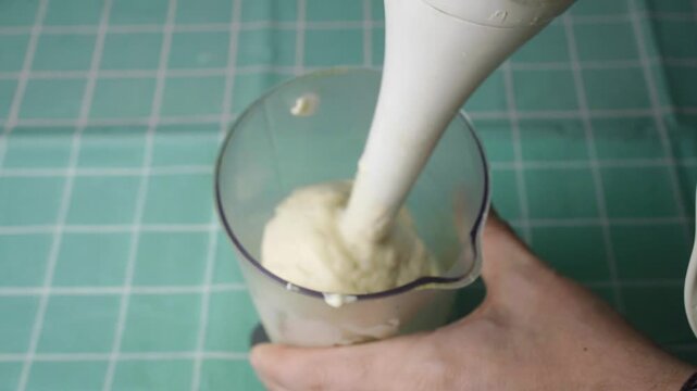 Hand blending fresh homemade mayonnaise with an immersion blender in a jar showing the final result