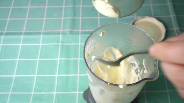 Freshly made creamy mayonnaise being served into a glass jar on wooden table