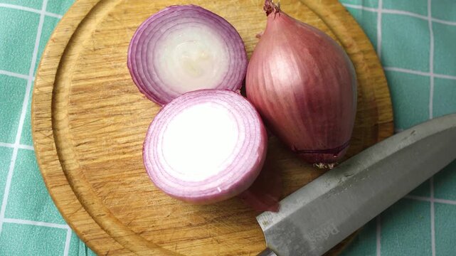 Close up view of a red onion halved next to a sharp knife on a wooden table