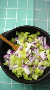 Vertical Close up of combining chopped onions and green chili peppers in a ceramic bowl