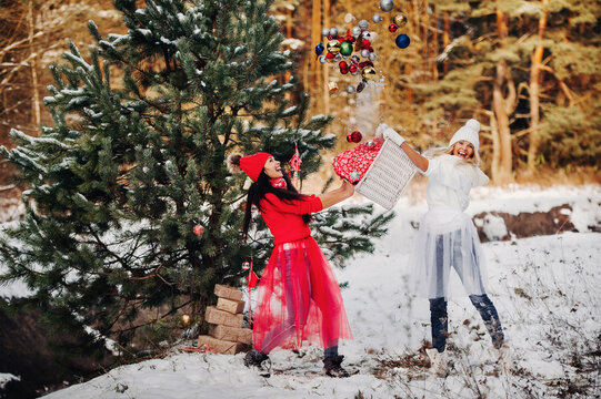 two girls near the Christmas tree throw a lot of toys on the tree. Christmas tree decoration on the street in winter.Lots of Christmas balls on the tree