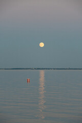 Full moon reflected on calm water with a navigational buoy at dusk © Levente Varga