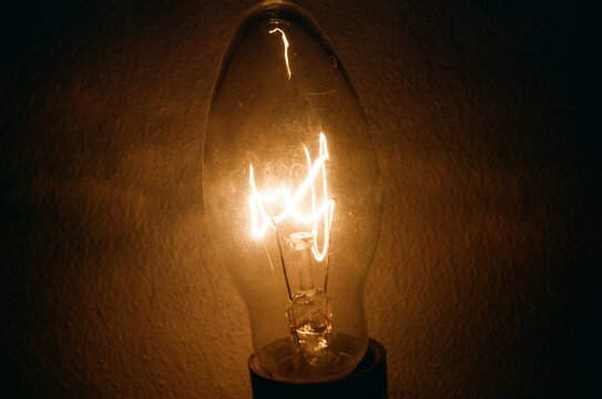 Close-up of the glowing filament of an illuminated vintage incandescent light bulb in the dark. Analog 35mm film.